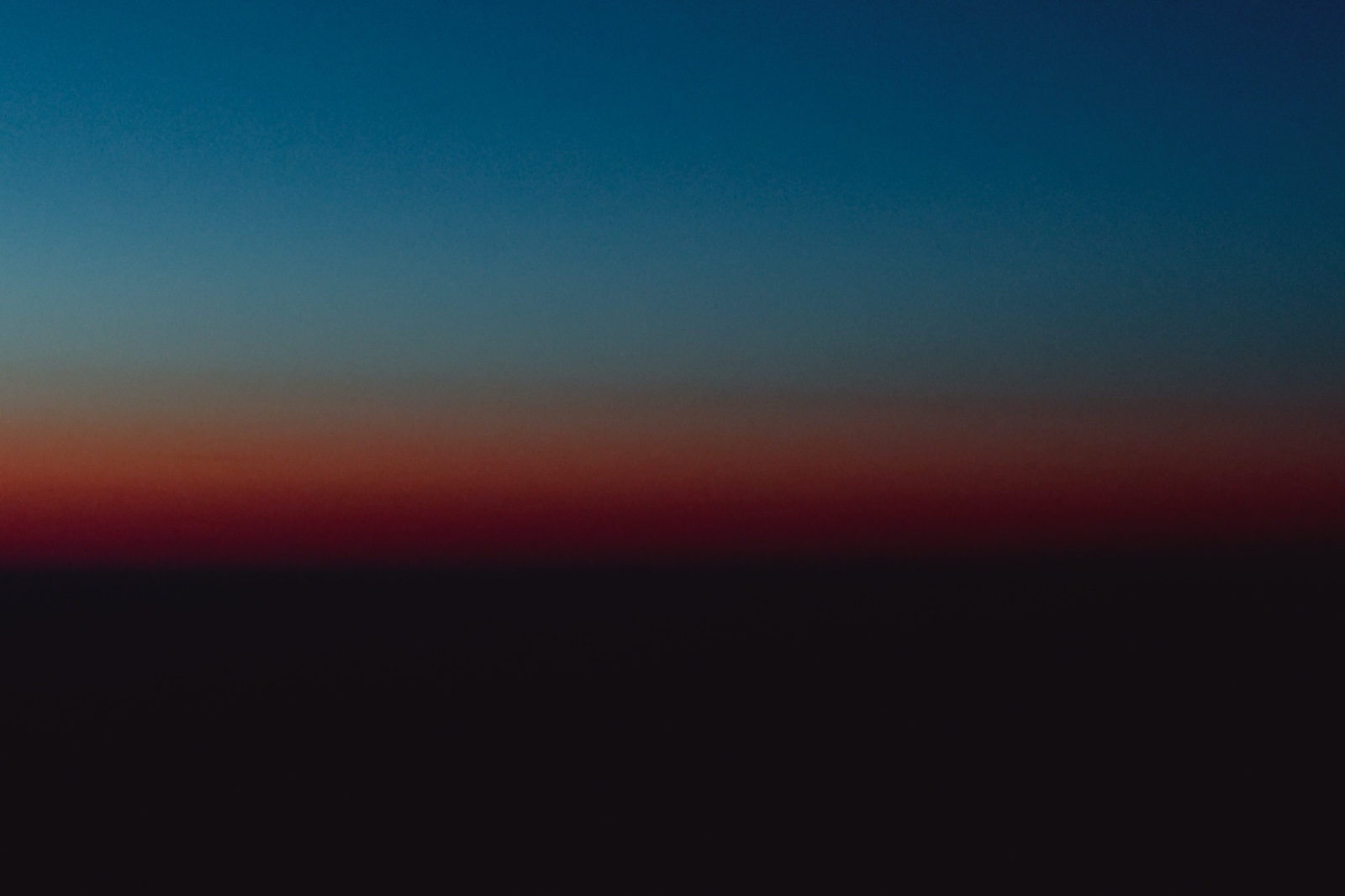 Una banda estrecha de rojo oscuro entre un cielo turquesa que se apaga y una masa negra, sin horizonte definido.